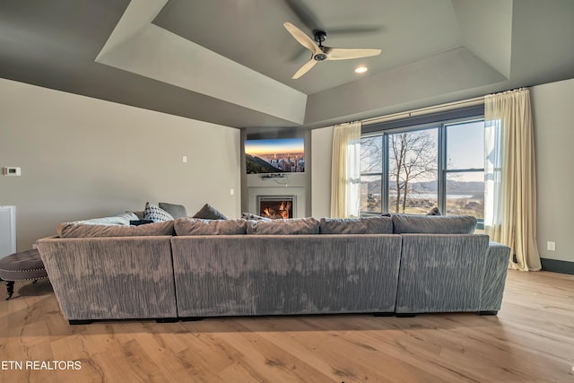 living room with a tray ceiling, ceiling fan, and light hardwood / wood-style flooring