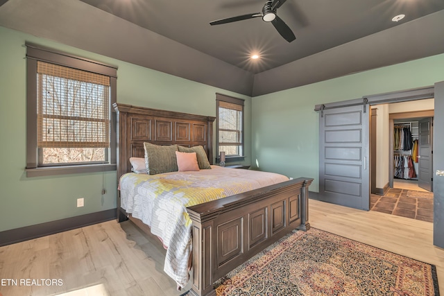 bedroom featuring lofted ceiling, ceiling fan, a barn door, light wood-type flooring, and a closet