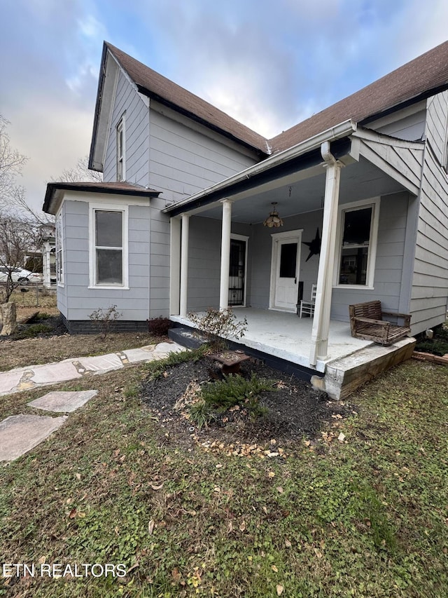 rear view of property featuring a porch and a lawn