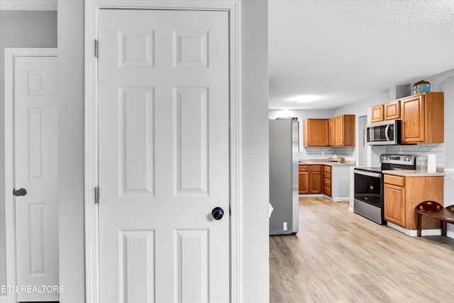 kitchen featuring decorative backsplash, a textured ceiling, appliances with stainless steel finishes, and light hardwood / wood-style flooring