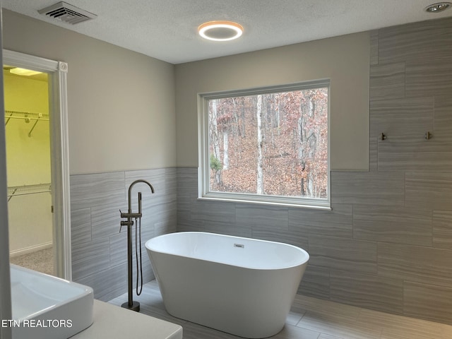 bathroom with a textured ceiling, a washtub, and tile walls