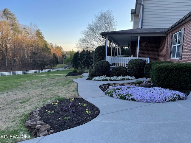 yard at dusk featuring covered porch and fence