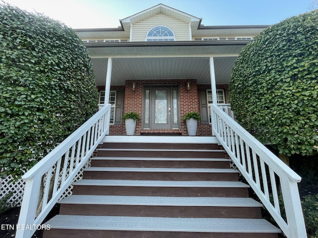 doorway to property with a porch and brick siding