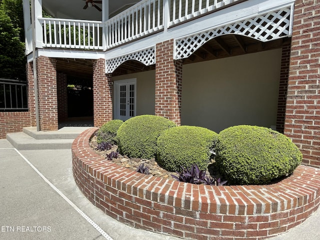 view of exterior entry featuring brick siding, a ceiling fan, french doors, and a balcony