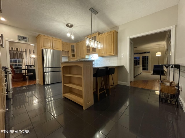 kitchen with a breakfast bar area, light brown cabinets, glass insert cabinets, and freestanding refrigerator