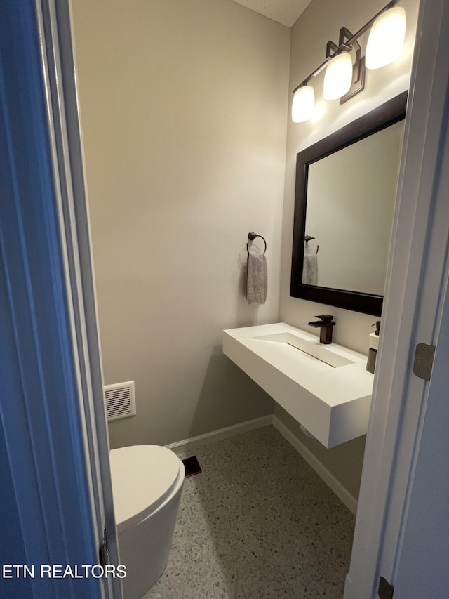half bath with baseboards, visible vents, toilet, and speckled floor