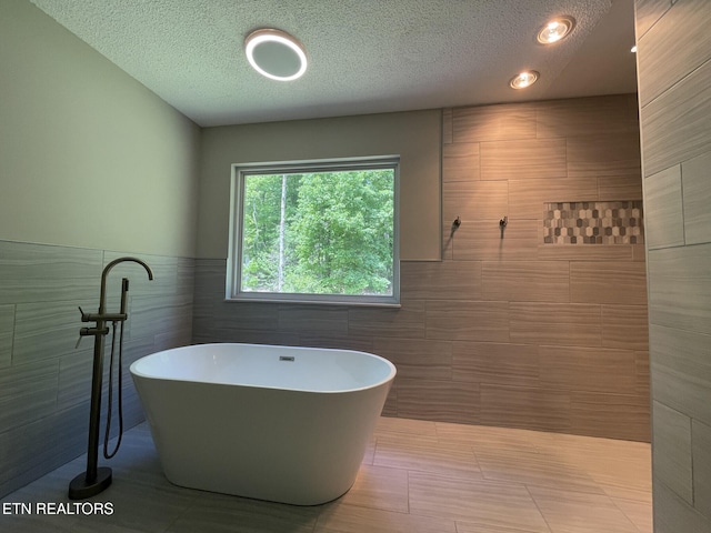 bathroom featuring tile walls, a freestanding bath, a wainscoted wall, and a textured ceiling