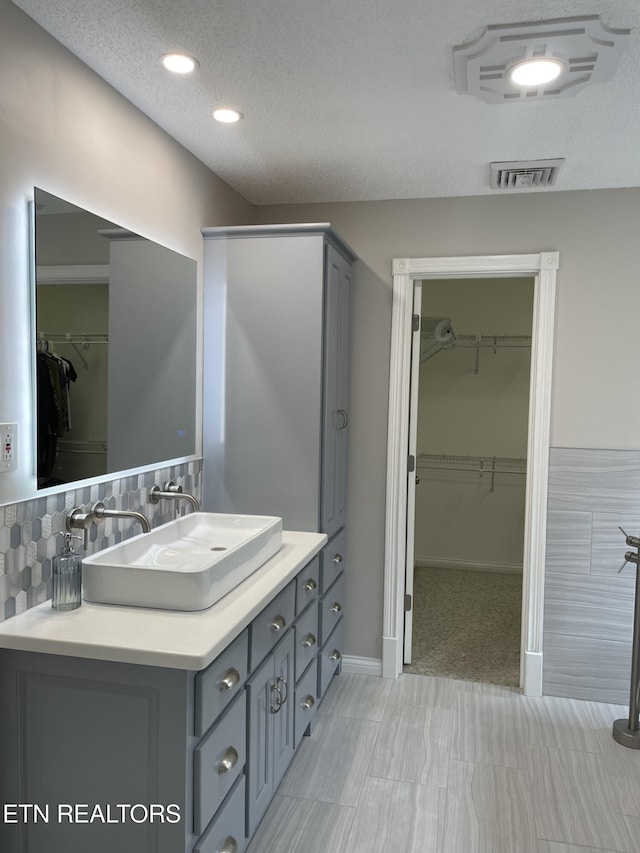 bathroom with a textured ceiling, a spacious closet, visible vents, baseboards, and vanity