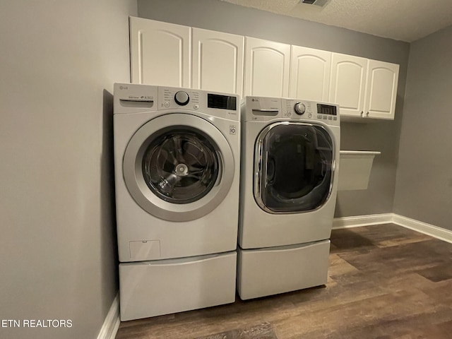 laundry room featuring dark wood-style floors, cabinet space, independent washer and dryer, baseboards, and a textured ceiling
