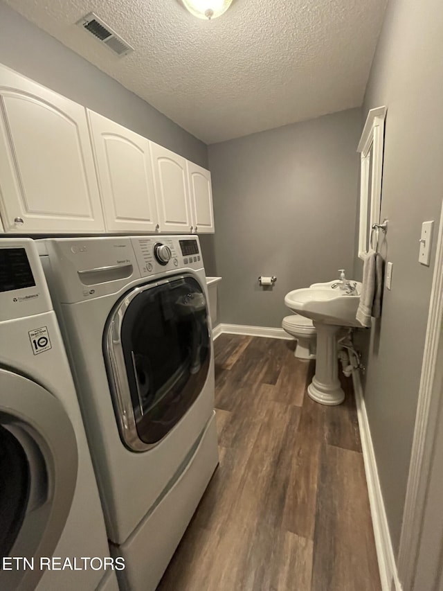 clothes washing area featuring separate washer and dryer, baseboards, visible vents, a textured ceiling, and dark wood-type flooring