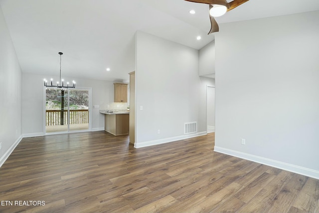 unfurnished living room with ceiling fan with notable chandelier, dark hardwood / wood-style floors, and vaulted ceiling