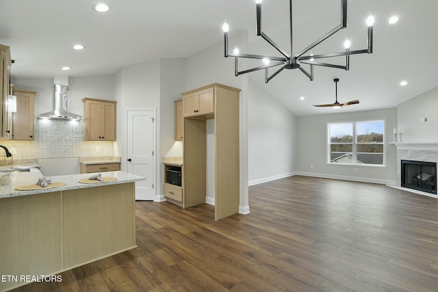 kitchen featuring light stone counters, a high end fireplace, light brown cabinetry, decorative backsplash, and wall chimney exhaust hood