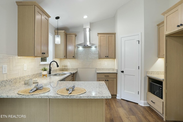 kitchen with pendant lighting, kitchen peninsula, light stone counters, and wall chimney exhaust hood