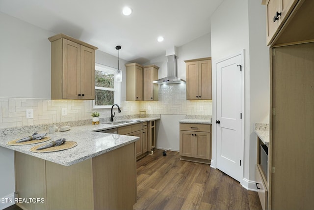 kitchen with sink, dark wood-type flooring, hanging light fixtures, kitchen peninsula, and wall chimney exhaust hood