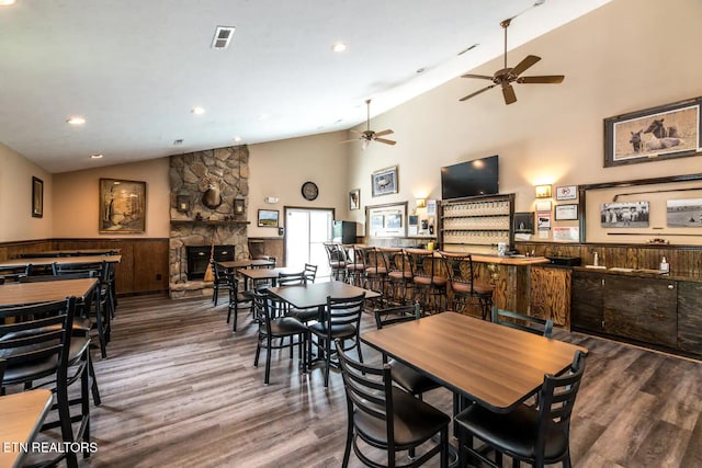 dining room with hardwood / wood-style floors, ceiling fan, a fireplace, and high vaulted ceiling