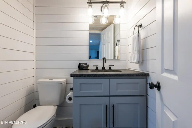 bathroom featuring vanity, toilet, and wood walls