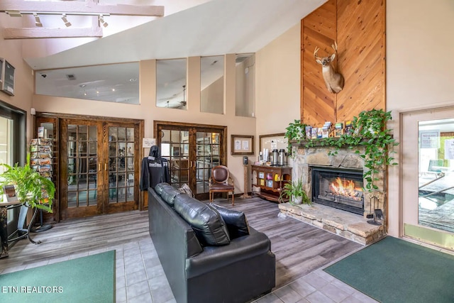 tiled living room featuring wood walls, a fireplace, high vaulted ceiling, and french doors