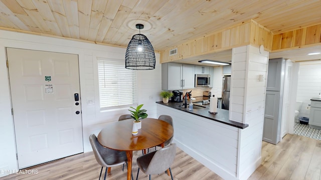 dining room with sink, light hardwood / wood-style flooring, wooden ceiling, and wood walls