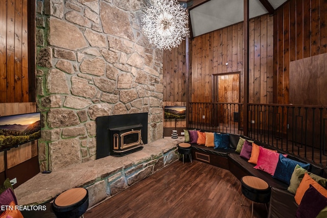 living room with lofted ceiling, a wood stove, an inviting chandelier, wooden walls, and hardwood / wood-style flooring