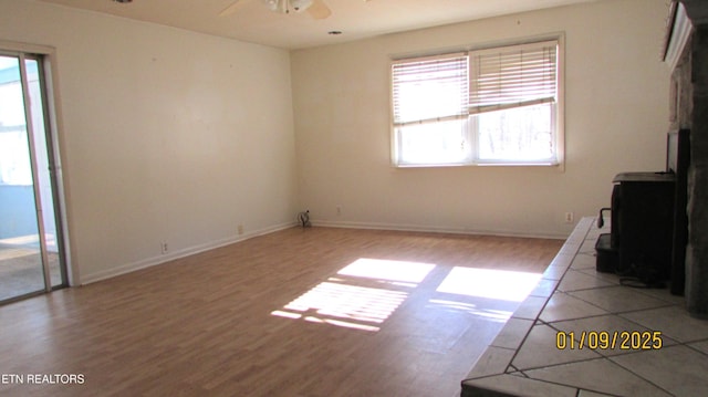 unfurnished living room with ceiling fan, light wood-type flooring, and a wood stove