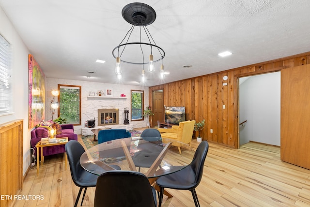 dining area featuring a stone fireplace, light hardwood / wood-style flooring, a chandelier, and a textured ceiling