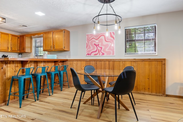 dining area with a textured ceiling, light hardwood / wood-style flooring, wood walls, and sink