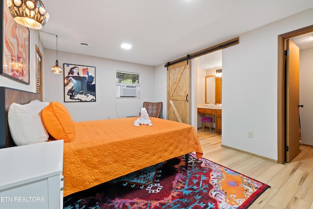 bedroom with light wood-type flooring, a barn door, ensuite bath, and cooling unit