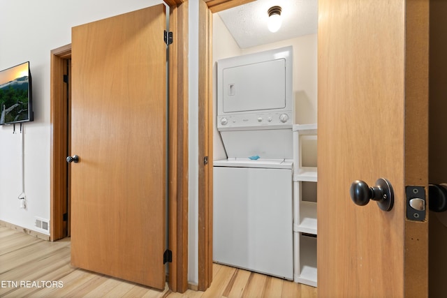 washroom with stacked washer and dryer, a textured ceiling, and light wood-type flooring