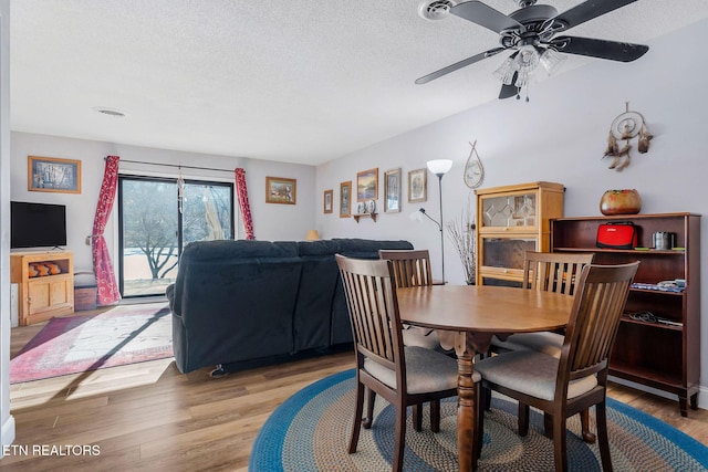 dining space with a textured ceiling, light wood-type flooring, and ceiling fan