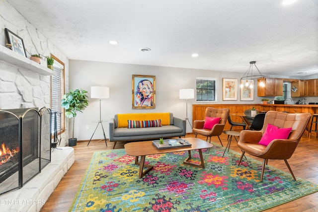 living room with light hardwood / wood-style floors, a stone fireplace, a textured ceiling, and a chandelier