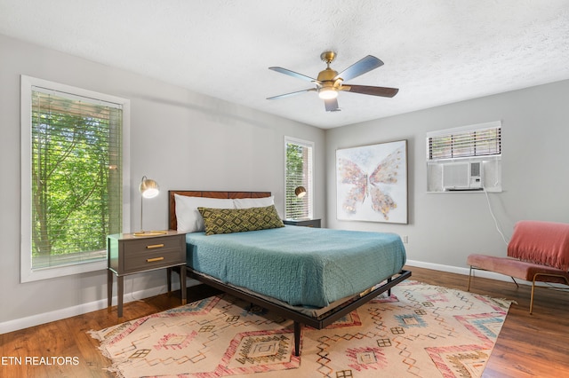 bedroom with a textured ceiling, hardwood / wood-style flooring, ceiling fan, and cooling unit