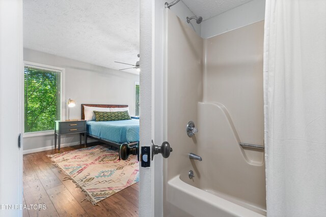 bathroom featuring ceiling fan, wood-type flooring, a textured ceiling, and shower / tub combo