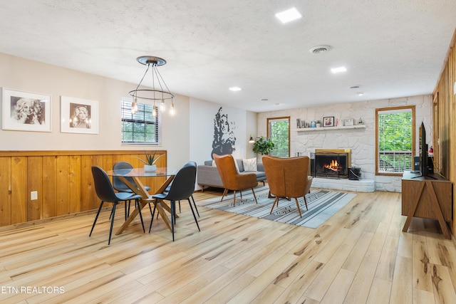 dining room with an inviting chandelier, a textured ceiling, wooden walls, a fireplace, and light wood-type flooring