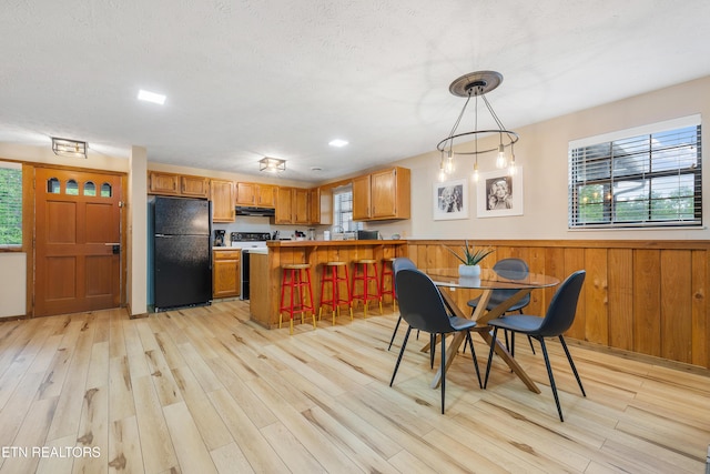 kitchen featuring light wood-type flooring, black fridge, wooden walls, decorative light fixtures, and a breakfast bar area