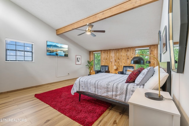 bedroom featuring ceiling fan, lofted ceiling with beams, wooden walls, and multiple windows