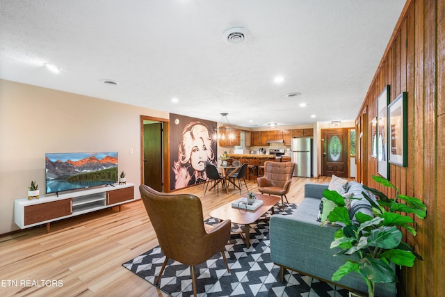 living room with light wood-type flooring, a textured ceiling, and wooden walls