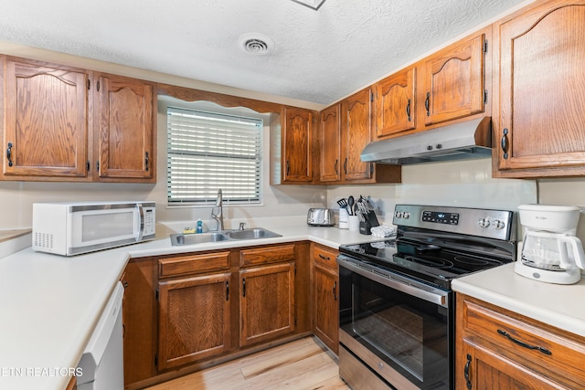 kitchen with a textured ceiling, light wood-type flooring, white appliances, and sink