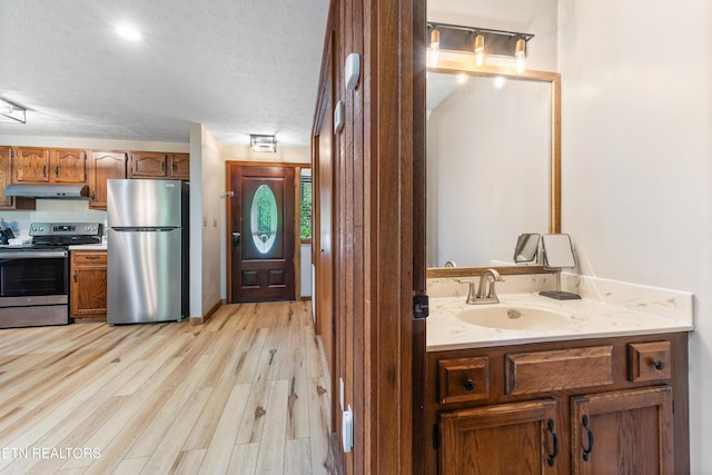 interior space with appliances with stainless steel finishes, a textured ceiling, light hardwood / wood-style floors, and sink