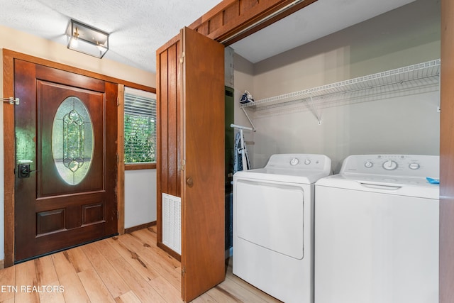 laundry room with light wood-type flooring, a textured ceiling, and washing machine and dryer