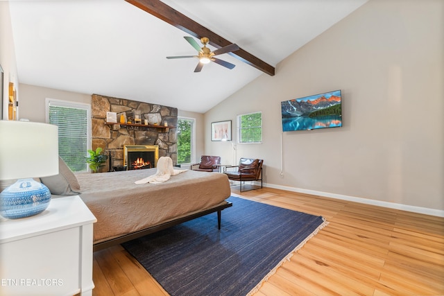 bedroom featuring vaulted ceiling with beams, ceiling fan, a stone fireplace, and wood-type flooring