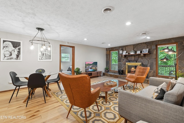 living room featuring a stone fireplace, light wood-type flooring, and a textured ceiling