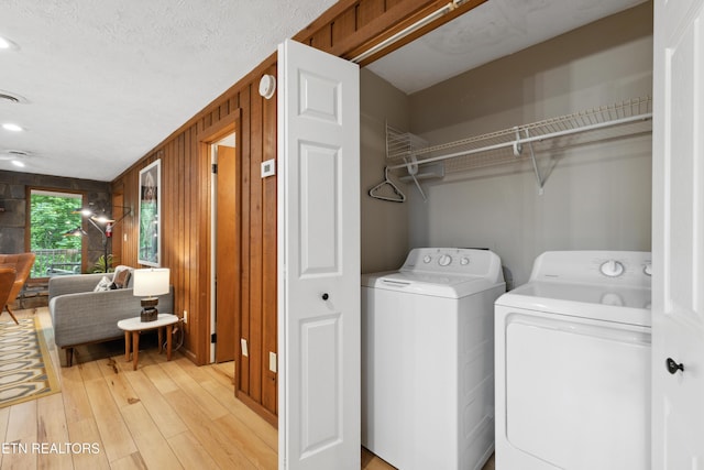 laundry area with wood walls, light hardwood / wood-style flooring, a textured ceiling, and independent washer and dryer