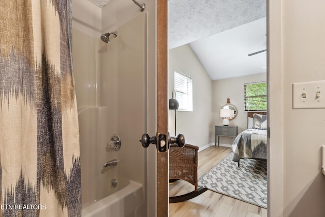 bathroom featuring lofted ceiling, hardwood / wood-style floors, shower / bathtub combination with curtain, and a textured ceiling