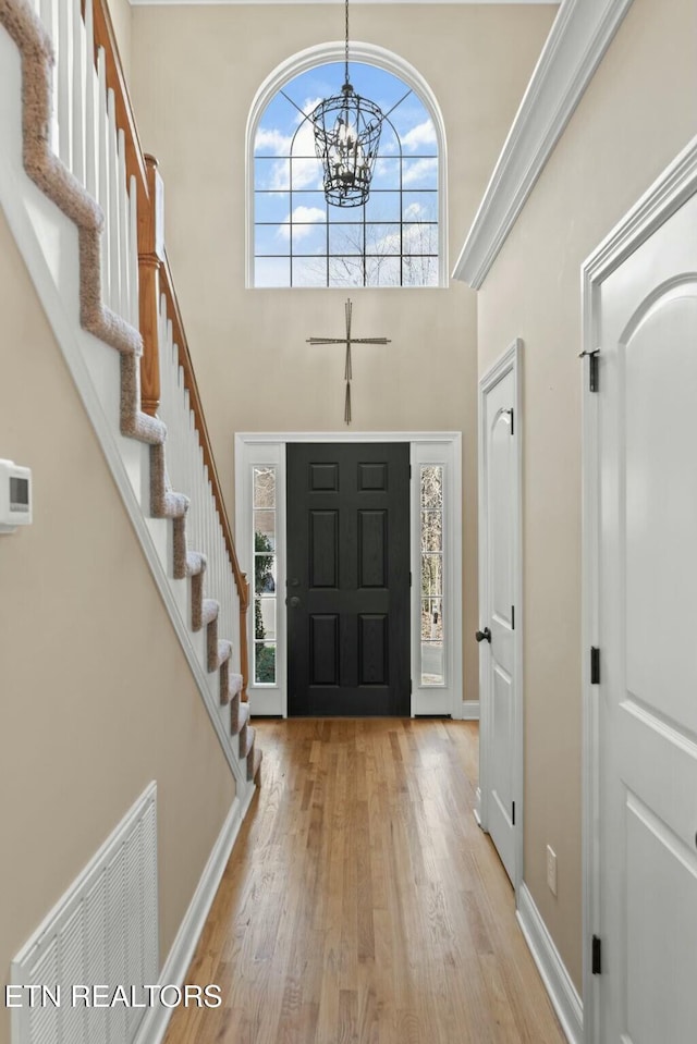 foyer entrance with a high ceiling, an inviting chandelier, light hardwood / wood-style floors, and crown molding