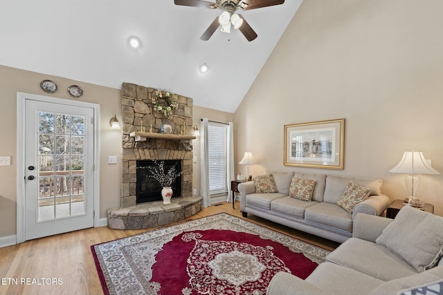 living room featuring light hardwood / wood-style floors, ceiling fan, a stone fireplace, and high vaulted ceiling