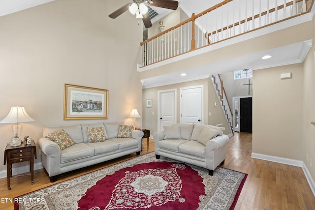 living room with a towering ceiling, hardwood / wood-style flooring, ceiling fan, and crown molding