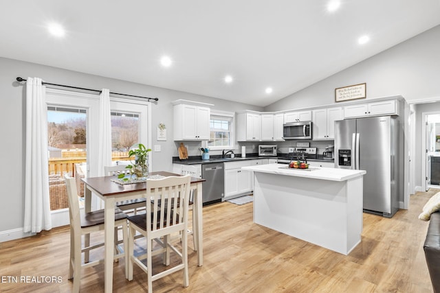 kitchen with stainless steel appliances, vaulted ceiling, white cabinets, and light hardwood / wood-style flooring