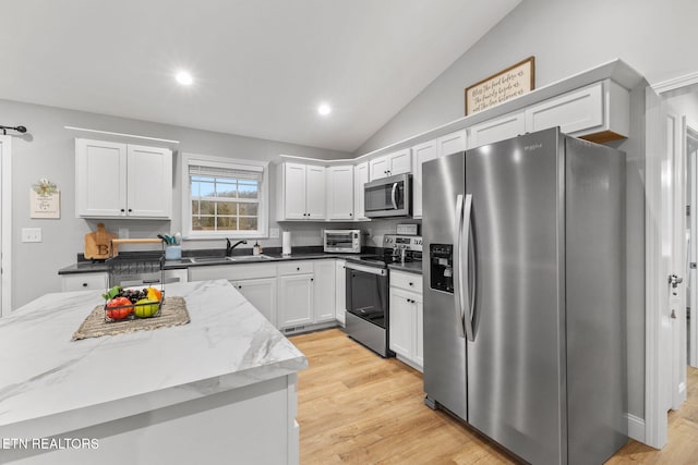 kitchen featuring vaulted ceiling, appliances with stainless steel finishes, white cabinetry, sink, and dark stone counters