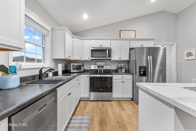 kitchen with lofted ceiling, sink, white cabinetry, appliances with stainless steel finishes, and light hardwood / wood-style floors