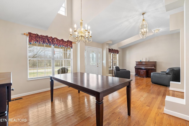 dining space featuring light wood-type flooring, an inviting chandelier, plenty of natural light, and vaulted ceiling